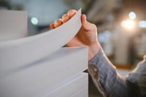 Close up of man putting stack of paper in printing machine at publishing shop, copy space